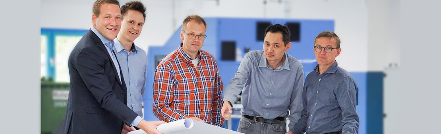 Gruppenbild mit fünf Personen in einer Druckerei, welche eine Papierrolle in der Hand halten.